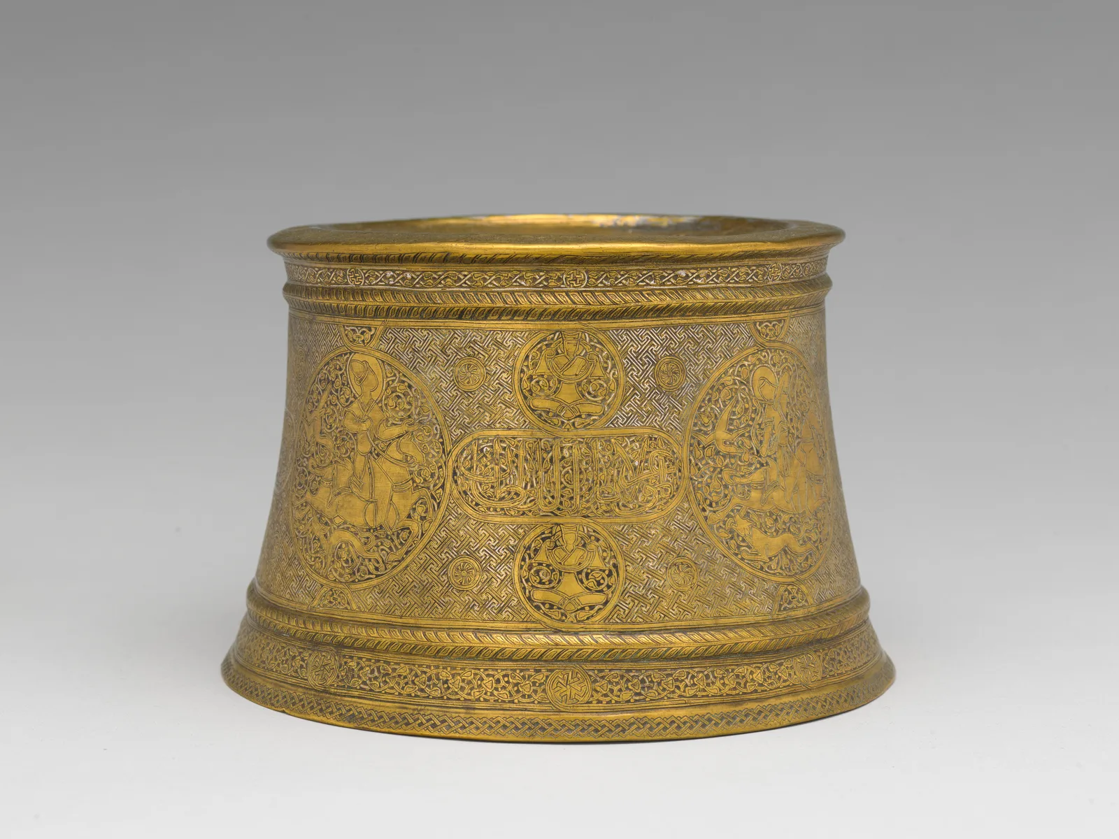 Cylindrical candlestick base with dense engraved ornament, medallions, inscriptions, and traces of silver inlay.